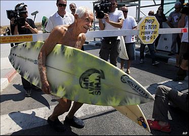 Doc Paskowitz ducking under a border crossing gate to deliver surfboards he had promised to Gazan surfers. (pic-surfing4peace.org/history)